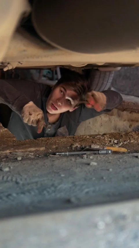 Man underneath a car reaching for a screwdriver for repairing car Stock Footage 346228712