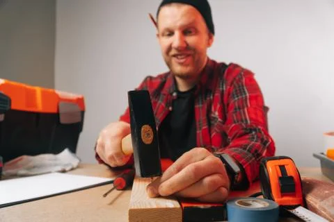A man in uniform clogs nails in a work carpentry. Focus on wooden hammer and  Stock Photos