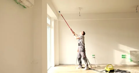 Man in uniform paints ceiling in white color with roller brush Stock Footage 321573558
