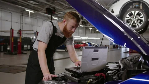 Man in uniform is using a laptop during car diagnostics.Car diagnostics station Stock Footage 240077369