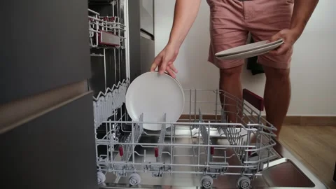 Man unloading clean white plates from a dishwasher in the kitchen Stock Footage 345833943