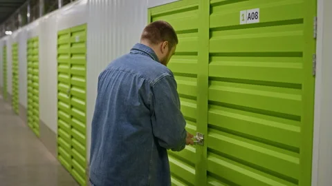 Man Unlocking Padlock on Metal Door of Self Storage Unit Stock Footage 340286178