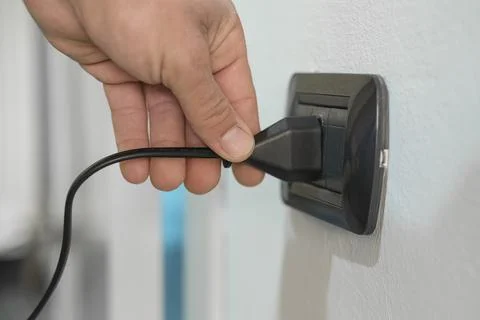 Man unplugging electronic device in wall power plug socket at home,energy costs Stock Photos