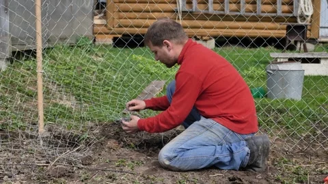 A man is unrolling the wire for a chain-link fence on his plot. Stock Footage 344698984