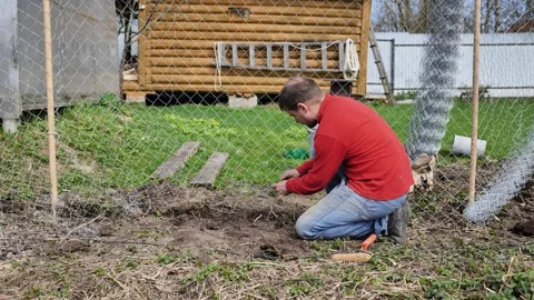 A man is unrolling the wire for a chain-link fence on his plot. Stock Footage 344699099