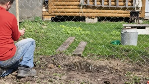 A man is unrolling the wire for a chain-link fence on his plot. Stock Footage 344699229