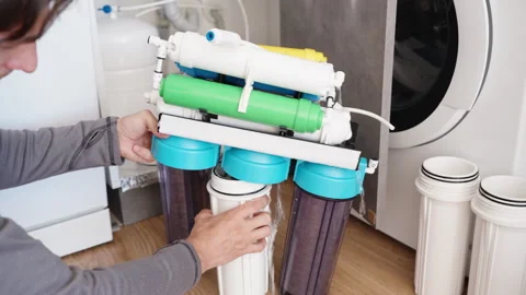 The man is unscrewing the housing to replace the water filter. It's a reverse os Stock Footage 250354551