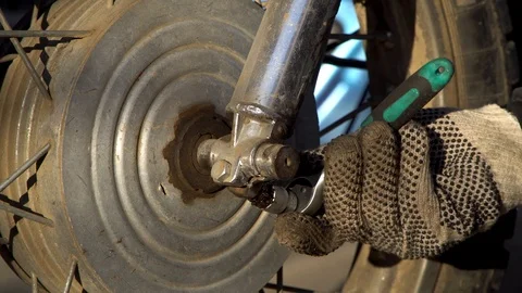 A man unscrews a bolt to remove a wheel from a motorcycle Stock Footage 123583382