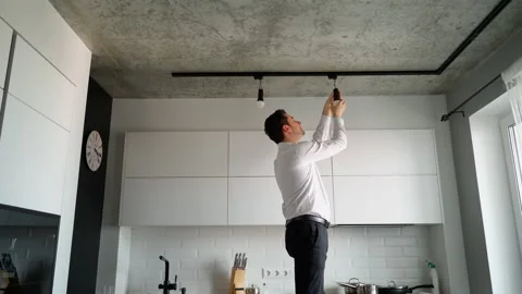 Man unscrews a light bulb from the base of modern track lighting Stock Footage 153290184