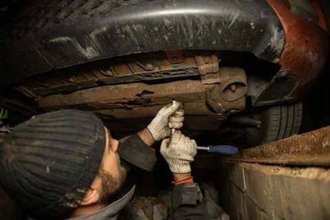 A man unscrews the nuts under the engine oil change machine in his garage. A man Stock Photos