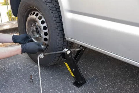 A man unscrews the nuts on the wheel to remove the wheel from the car Stock Photos