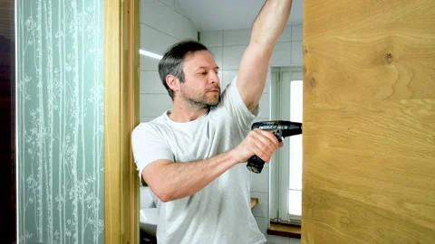 Man unscrews a screw with a screwdriver. The master removes a wooden door Stock Footage 194037544