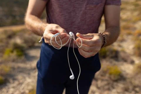 A man untangles the cable of a pair of white headphones to listen to music Stock Photos