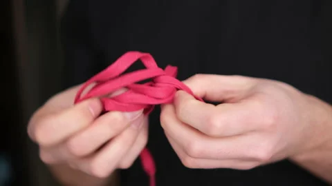 A man untangles a red string, hands close-up on a blurry background. The backgro Stock Footage 146830856