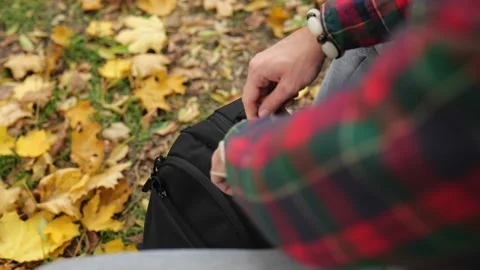 A man unzips a black backpack in an autumn park Stock Footage 220415081