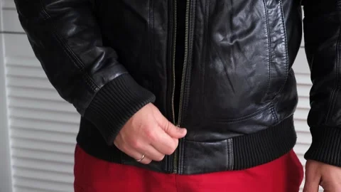 The man unzips his leather jacket. Metal zipper. A man in outerwear. Biker or Stock Footage 323766086
