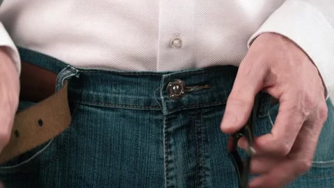 Man unzips zipper and button on blue jeans and unbuckles leather belt. closeup. Stock Footage 245260796