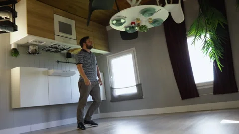A man in an upside-down house interacts with kitchen fixtures Видео 283079090