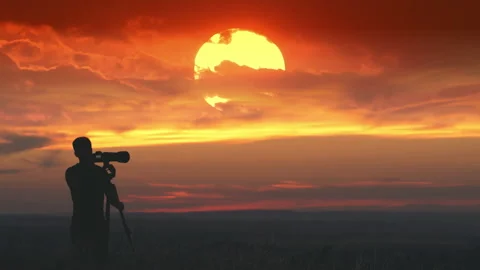 The man use the camera with tripod against the amazing red sun background Stock Footage 133722021
