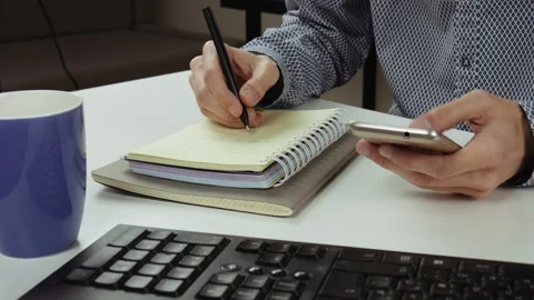 A man use his smartphone and taking notes in notebook at work. Stock Footage 101700660