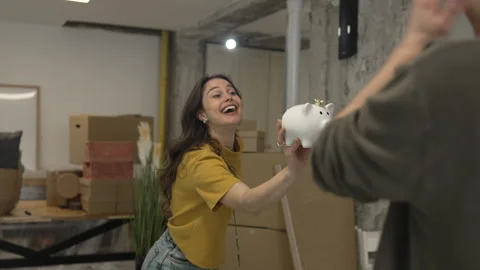 Man use mobile phone for shooting woman with piggy bank around boxes Stock Footage 308630422