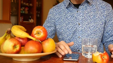 A Man use Mobile Smart Phone at the Table, eats Apple at Home Stock Footage 124650888