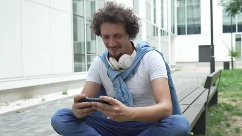 Man use mobile smart phone play video games sit outdoor Stock Footage 248305152