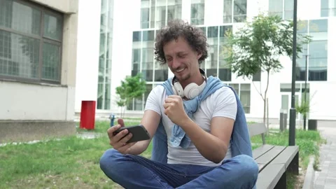Man use mobile smart phone play video games sit outdoor Stock Footage 248305157
