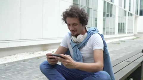 Man use mobile smart phone play video games sit outdoor Stock Footage 248305158