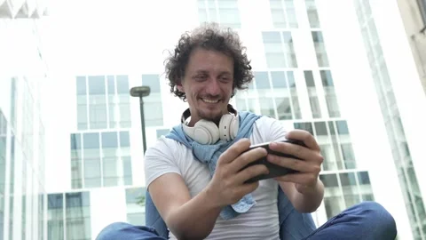 Man use mobile smart phone play video games sit outdoor Stock Footage 248305563