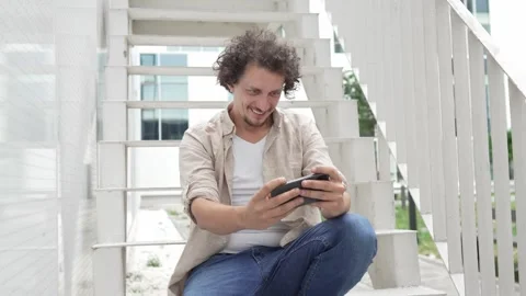 Man use mobile smart phone play video games sit outdoor Stock Footage 248305856
