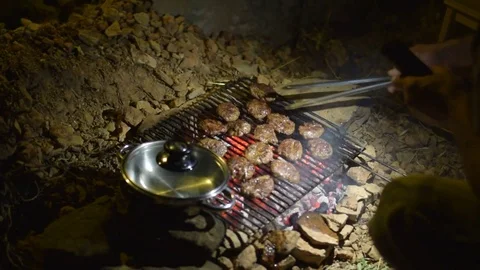 Man use phone light to lighting burgers on grill, campfire, at night             Stock Footage 77842080