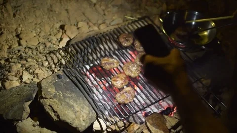 Man use phone light to lighting burgers on grill, campfire, at night             Stock Footage 77845883