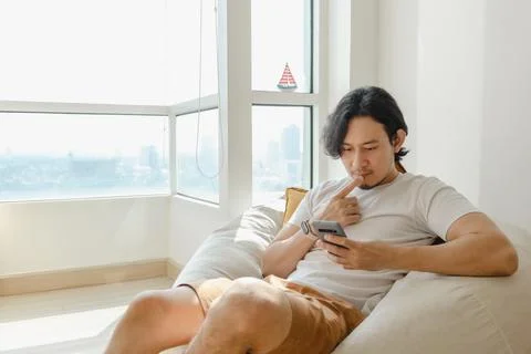 Man use smartphone while sit and relax on bean bag sofa in his apartment. Stock-Fotos
