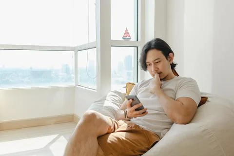 Man use smartphone while sit and relax on bean bag sofa in his apartment. Foto stock