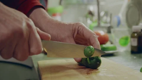 A man uses a chefs knife to slice green cucumber on a wooden board in kitchen 스톡 동영상 321604108