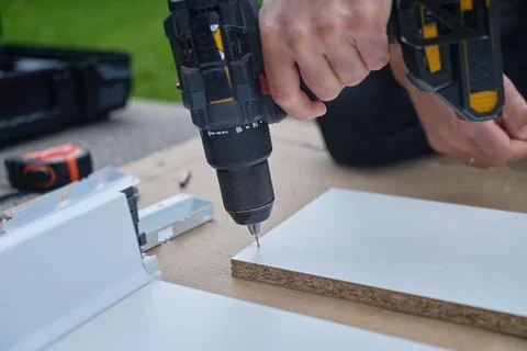 Man uses cordless drill to make hole in furniture board during DIY assembly Stock Photos