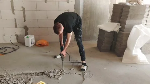 Man uses drill to work on building site with construction materials around him Stock Footage 328138843