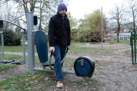 Man uses exercise machine in a park amid fallen leaves and trees Stock Photos