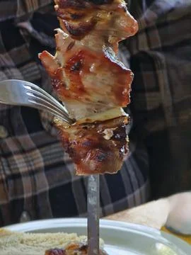 A man uses fork to remove freshly grilled pork with onions from a skewer. C.. Stock Photos