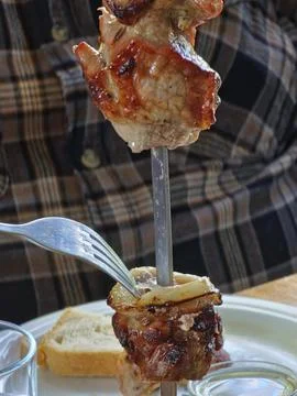 A man uses a fork to remove freshly grilled pork with onions from skewer. Clo Stock Photos