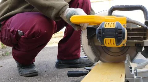 A man uses a hand-held circular saw to saw a light-colored wooden board Stock Photos