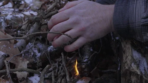 A man uses his hands to shield the tiny flames from the wind as he begins Stock Footage 265159561