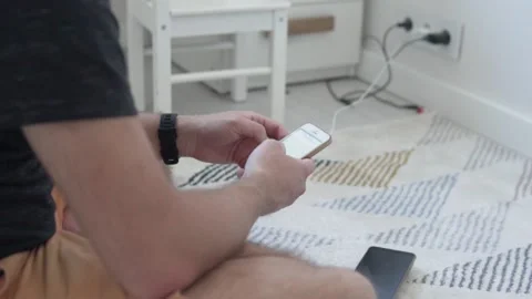 The man uses his mobile phone at home on the floor next to the socket for Stock Footage 133248329