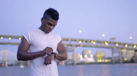 Man Uses His Smart Watch By River With City Lights In Background Stock Footage 67970966