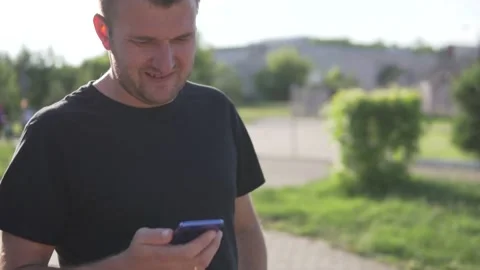 A man uses a mobile phone outside while walking in a park in the summer Stock Footage 134676448