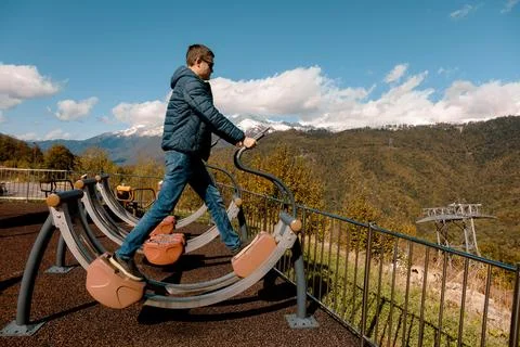 Man uses outdoor exercise machine on mountain with snow-capped peaks Stock Photos