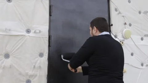 Man uses a paint roller to apply fresh black protective coating to an exter.. Stock Footage 345411980