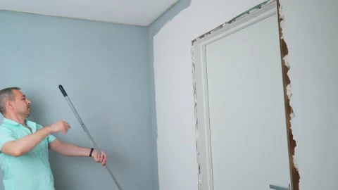 A man uses a paint roller to paint the wall gray Stock Footage 196812603