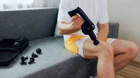 Man uses a percussion massage gun on his thigh for post-workout recovery and myo Video stock 342599275